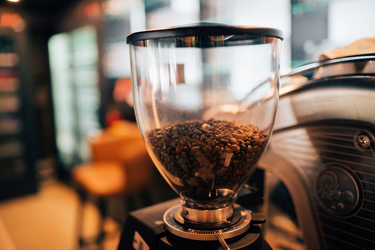 Burr coffee grinder beside scattered roasted coffee beans