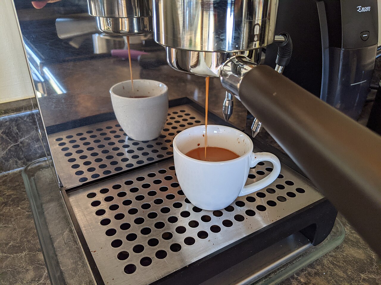 Home espresso machine pulling a shot into a small cup